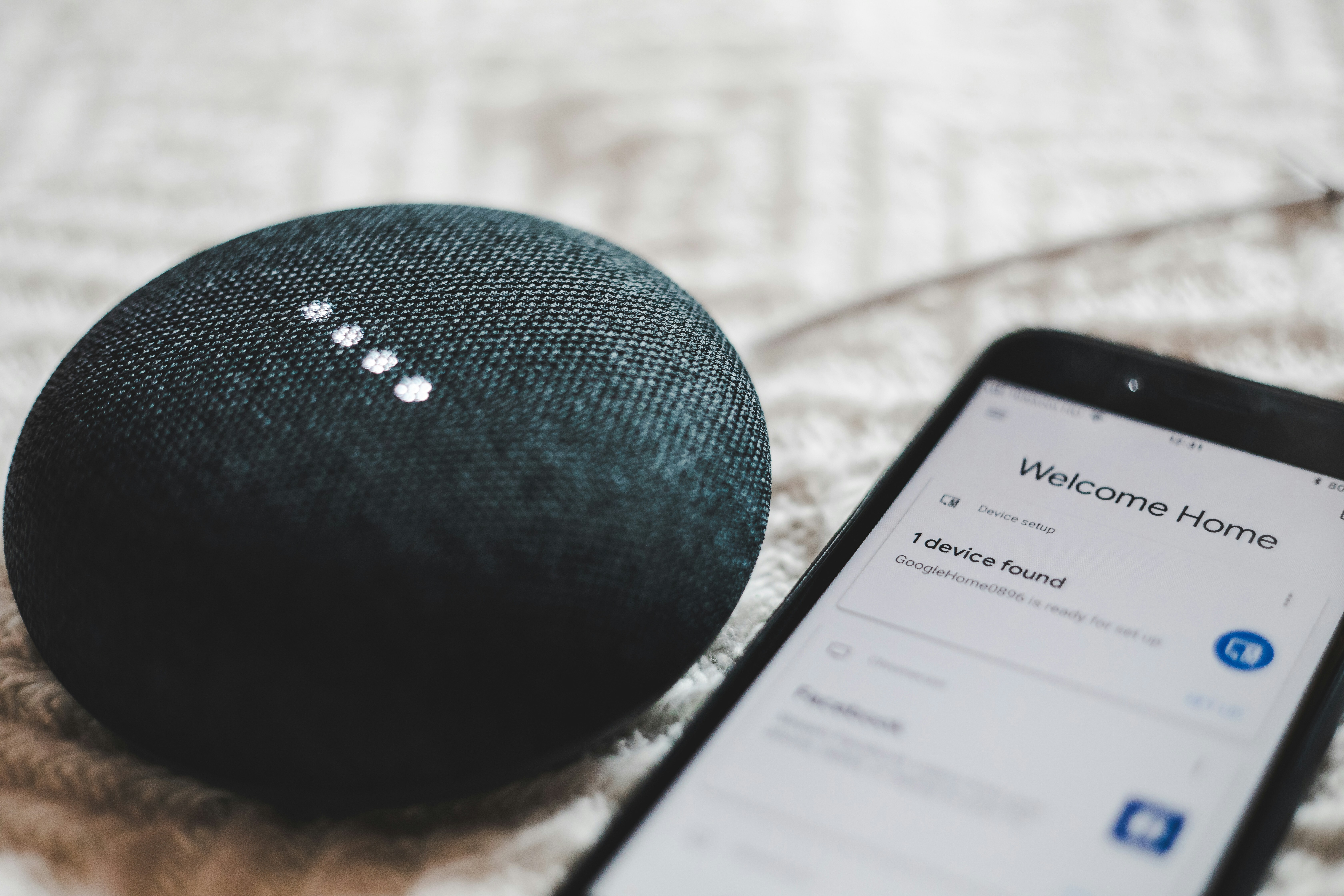 Photograph of turned-on Google Home Mini and smartphone with Google Home app open on-screen.