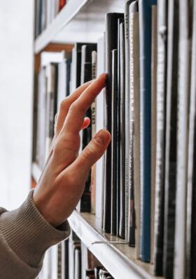 A row of books with a hand searching