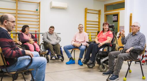 A group of people, including people with disabilities, sit in a community hall
